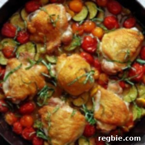 An overhead shot of a skillet filled with crispy chicken thighs, cherry tomatoes, zucchini, and basil