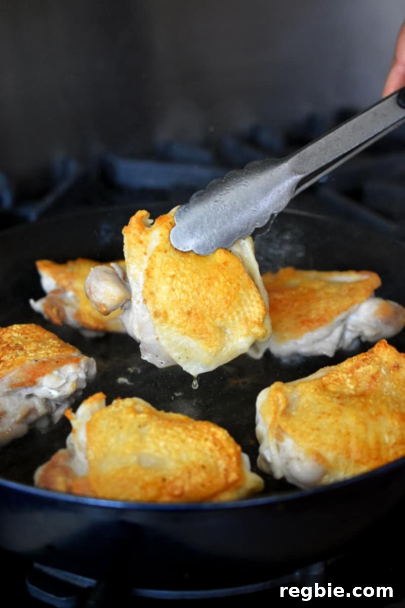 A pair of tongs flipping crispy chicken thighs to cook on the meaty side in a skillet