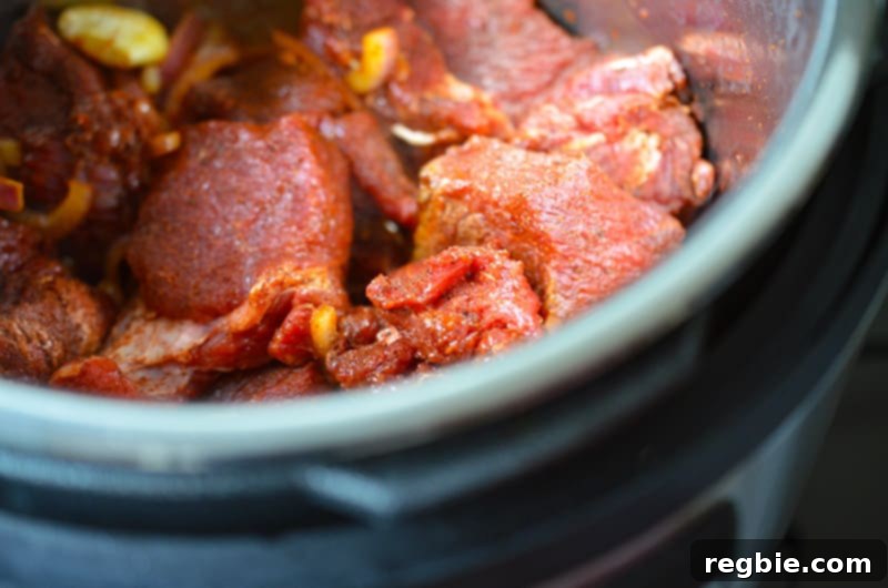 A closeup image of the seasoned beef being incorporated into the Instant Pot, ready for the liquids.