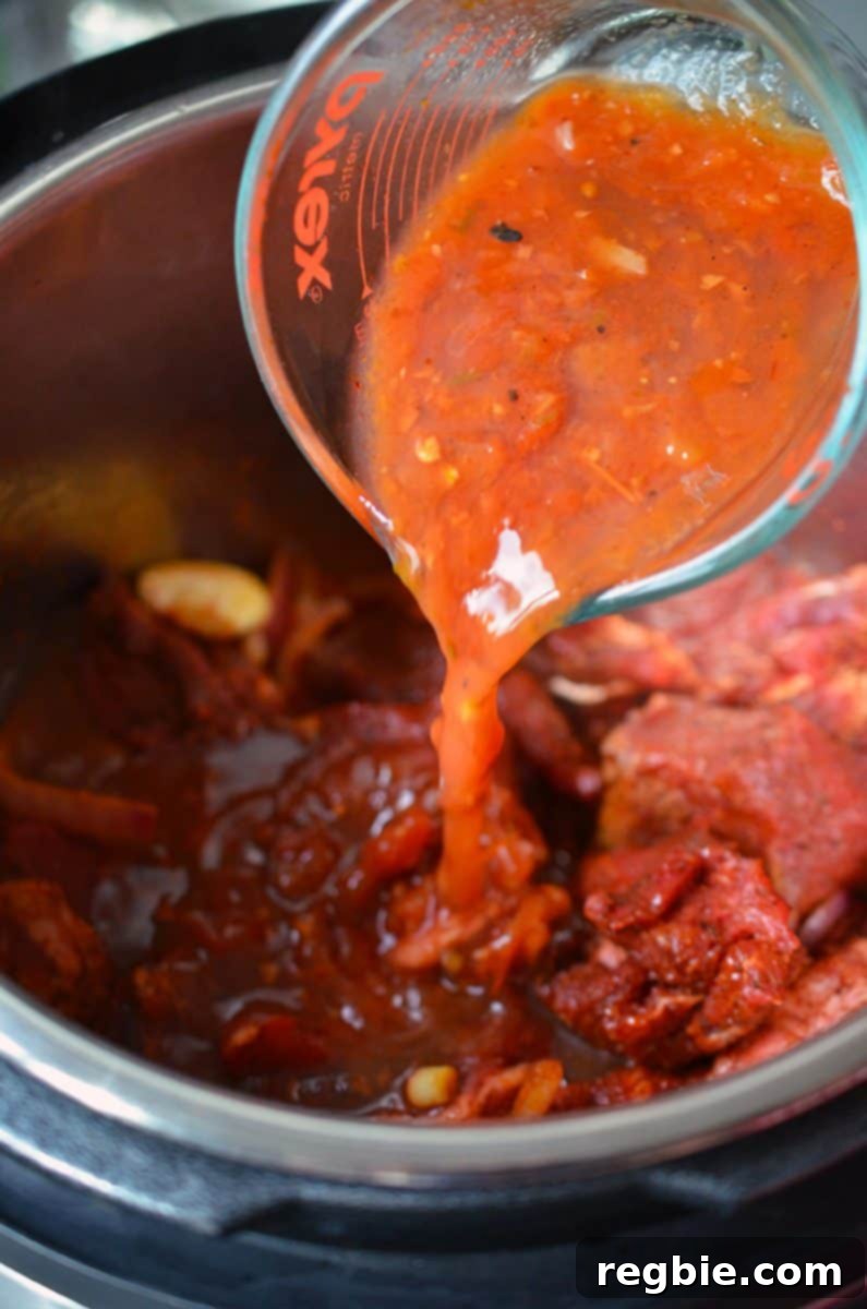 Roasted tomato salsa is poured over the beef and aromatics in the Instant Pot, adding a rich, tangy liquid component.