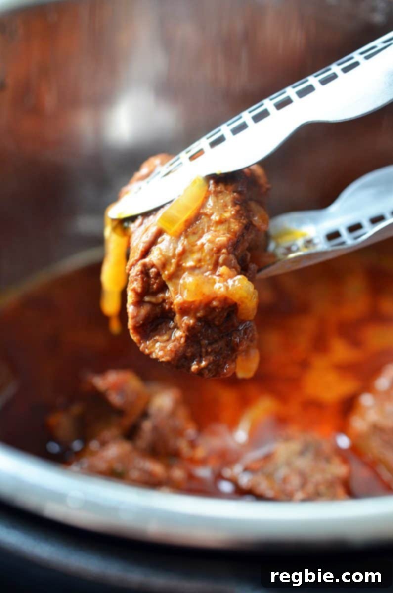 A pair of tongs has picked up a piece of perfectly cooked Instant Pot Mexican Beef from the Instant Pot, demonstrating its shreddable texture.