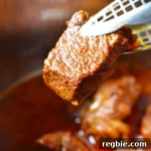 A pair of tongs is holding a piece of fork tender Instant Pot Mexican Beef