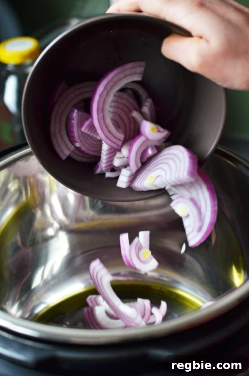 Sliced red onions are added to an Instant Pot with melted ghee, beginning to soften.