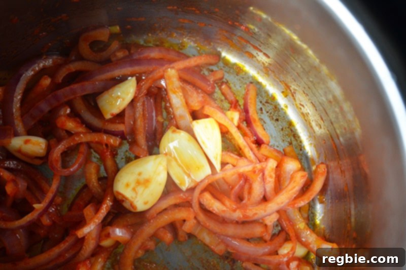 Peeled garlic cloves are added to the sautéed onions and tomato paste in the Instant Pot for an aromatic boost.