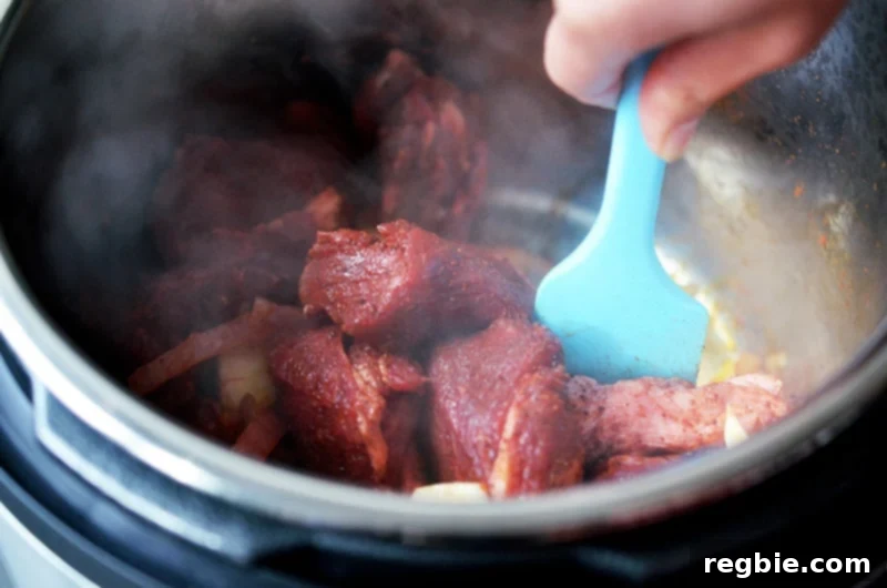 The seasoned beef is stirred into the Instant Pot, mixing with the flavorful onion and tomato base.