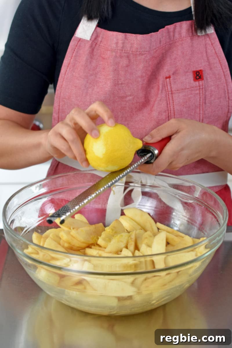 Guilt Free Apple Crisp 15 Adding lemon zest to a large bowl filled with seasoned sliced apples.