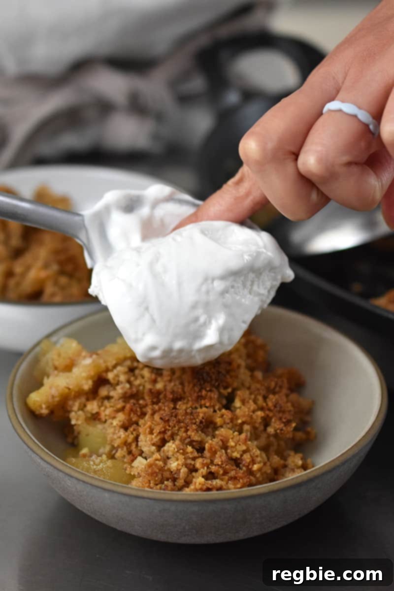 Guilt Free Apple Crisp 4 Topping a shallow bowl filled with paleo apple crisp with whipped coconut cream.