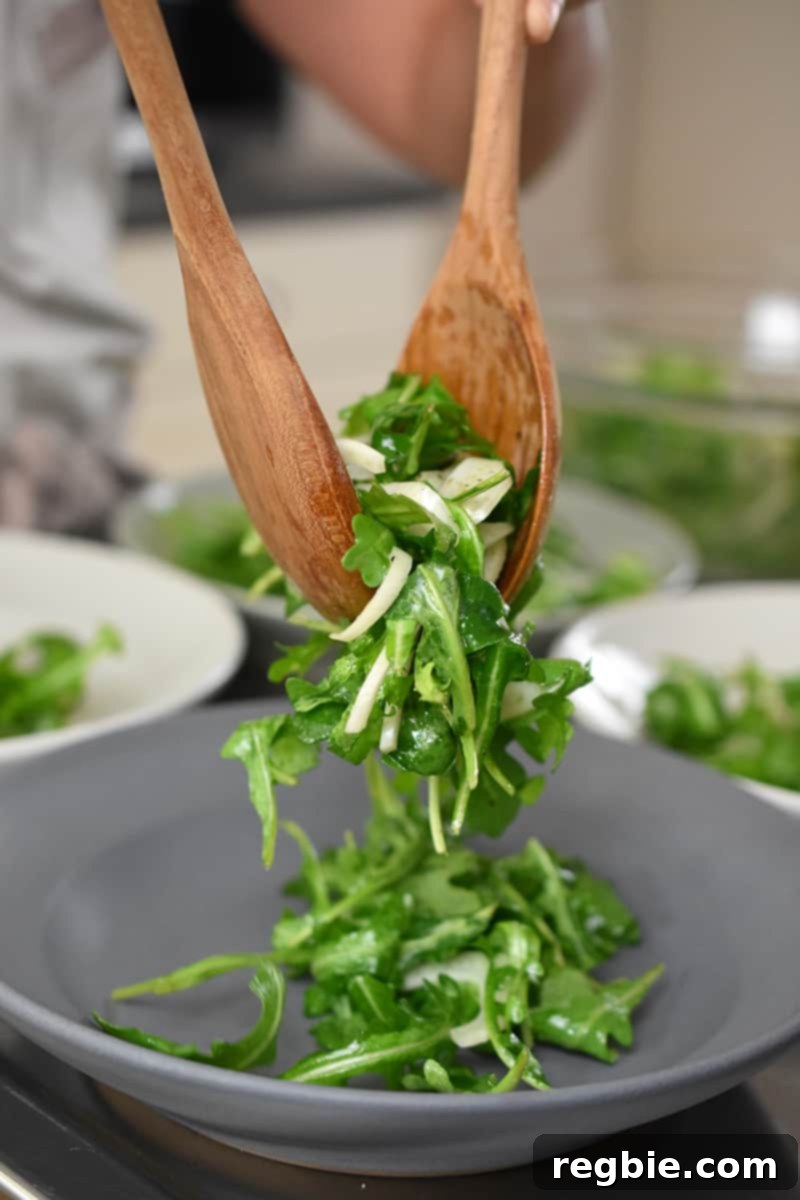 Two wooden spoons are dividing salad greens onto a gray shallow bowl.