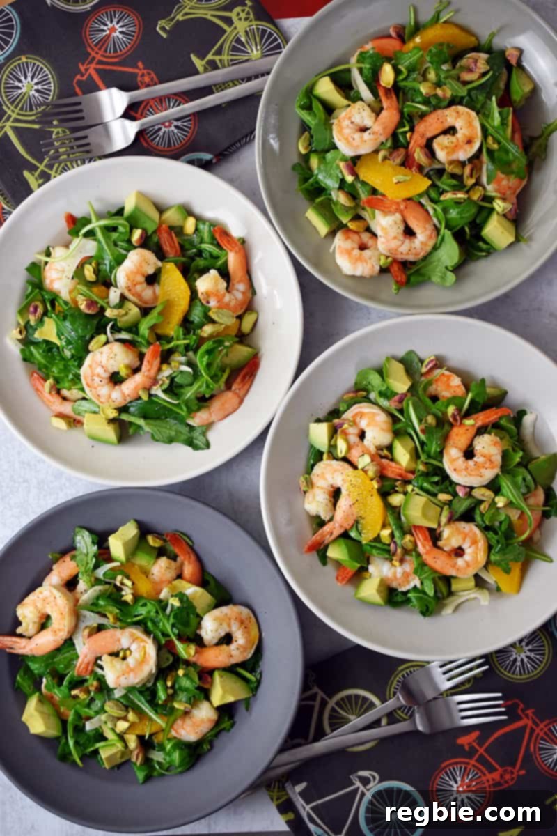 An overhead shot of four bowls of shrimp and avocado salad with fennel, arugula, orange segments, and pistachios.