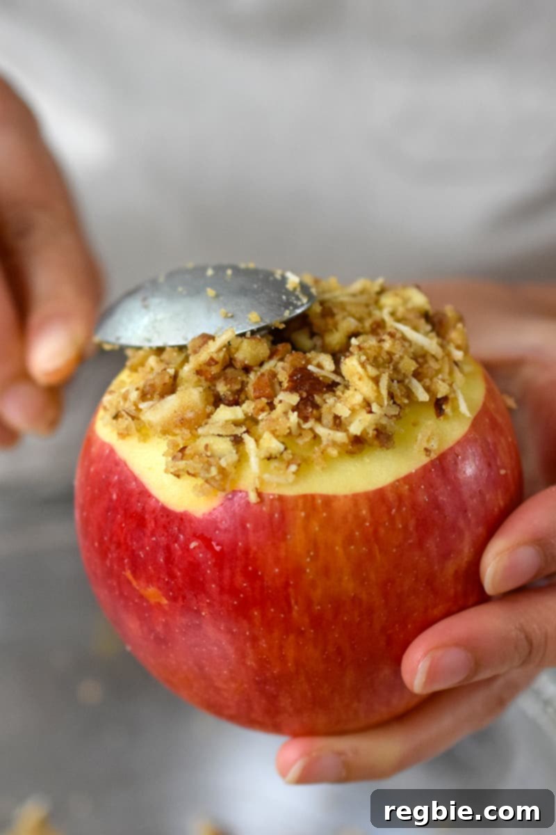 Wholesome Spiced Baked Apples 15 A spoon is adding baked apple filling to the top of an apple, covering the unpeeled portion.