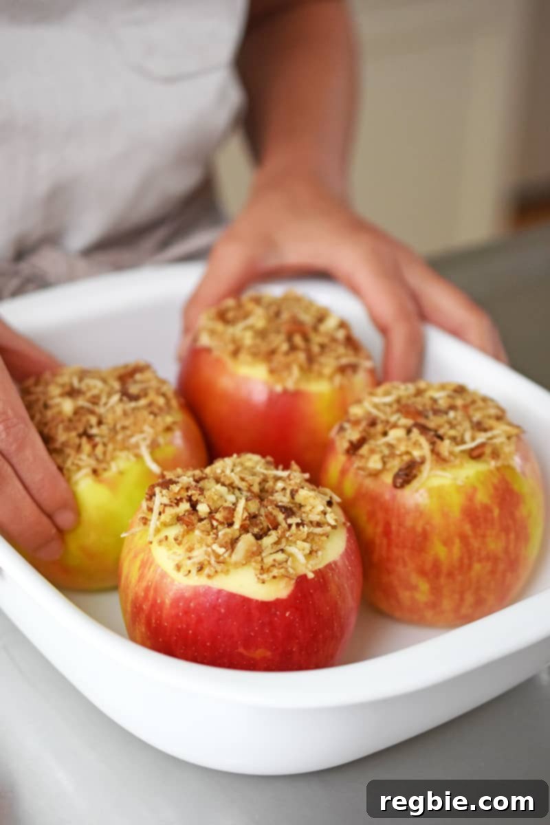 Wholesome Spiced Baked Apples 16 Two hands are placing stuffed apples into a white baking dish.