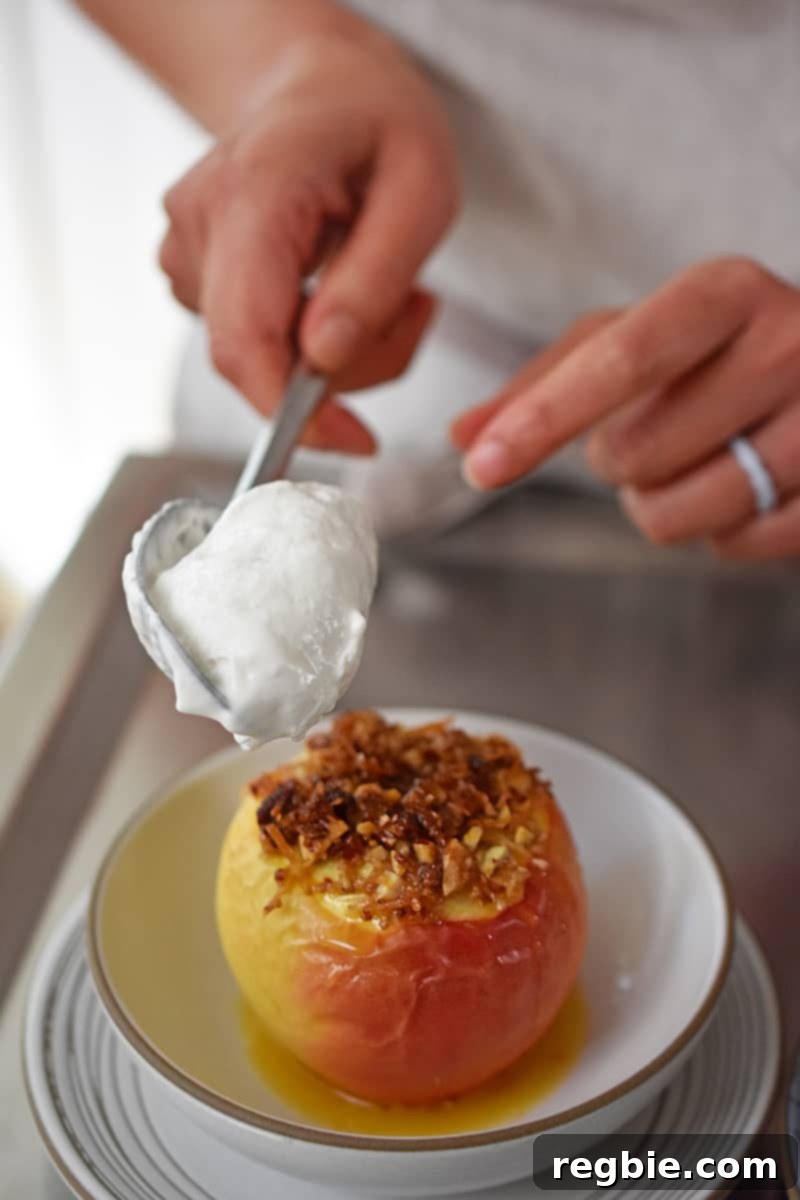 Wholesome Spiced Baked Apples 22 A spoon is adding a dollop of whipped cream to a baked apple in a shallow white bowl.
