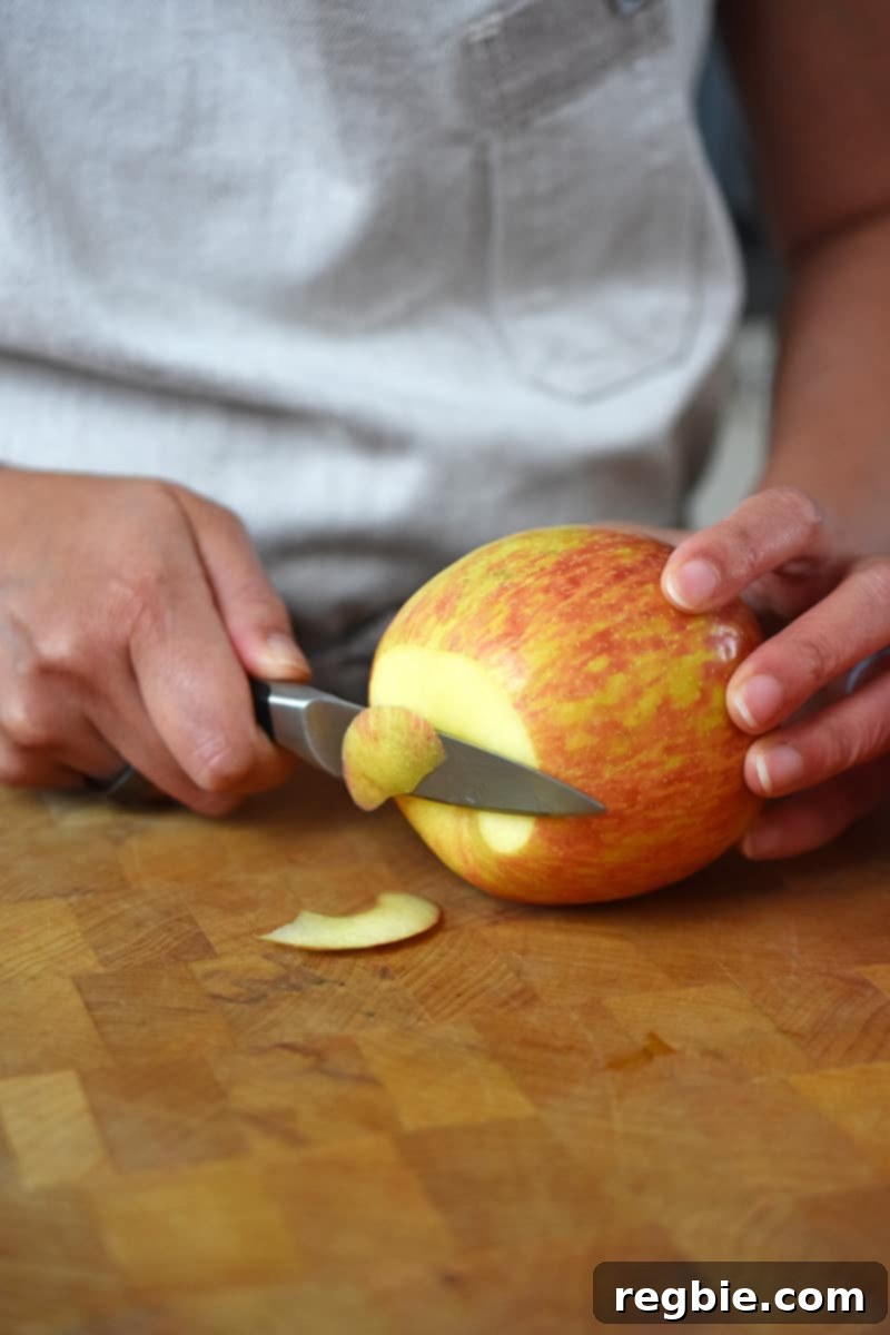 Wholesome Spiced Baked Apples 6 Someone using a paring knifer to trim the bottom of the apple on a wooden cutting board.