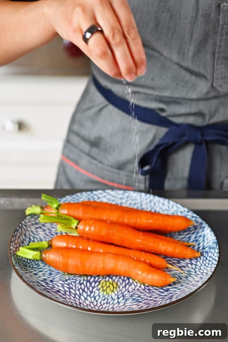 Golden Roasted Air Fryer Carrots 5 Sprinkling salt on some carrots on a blue and white plate.