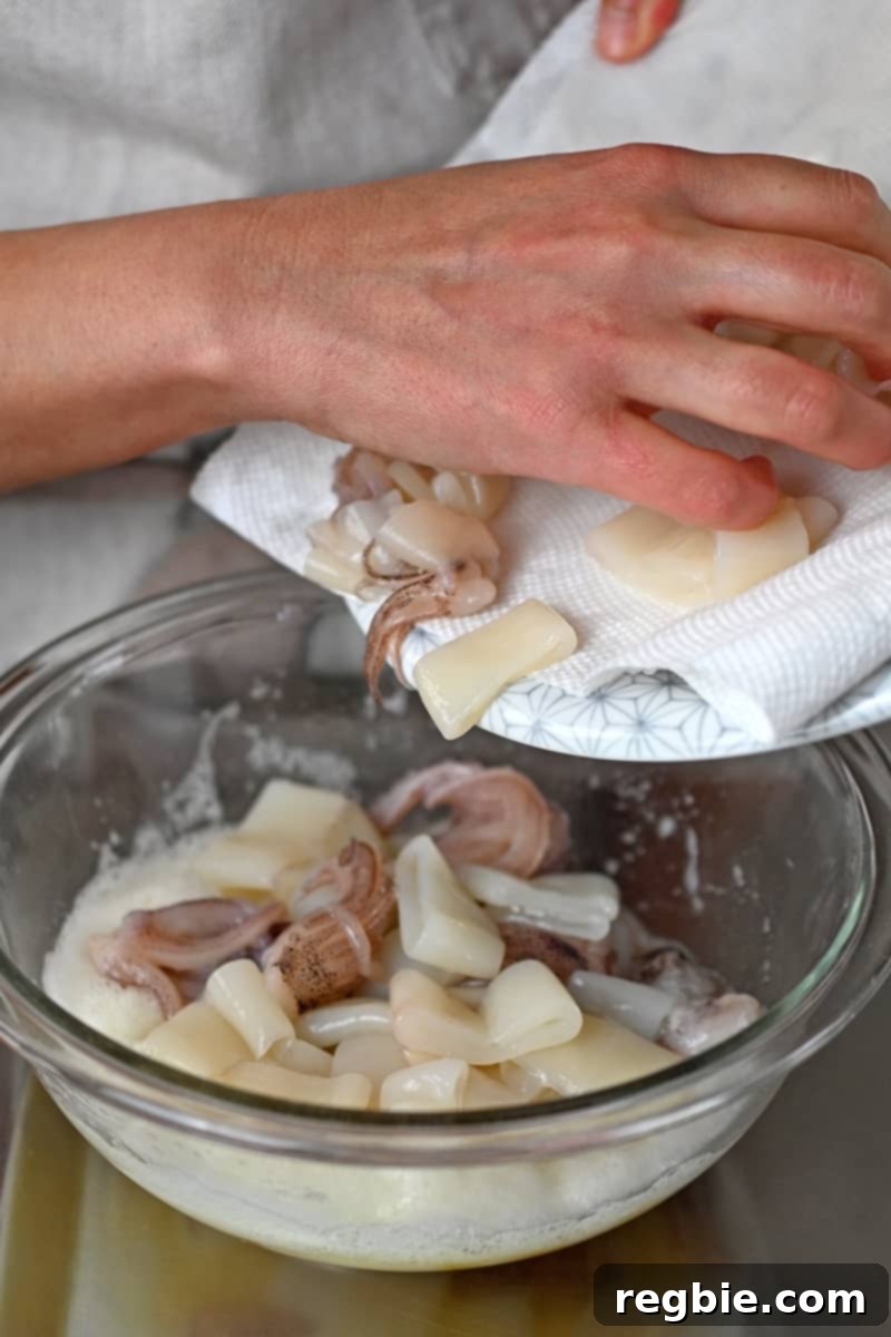 Adding the calamari to a bowl filled with whisked egg whites, ensuring each piece is ready for the flour coating.