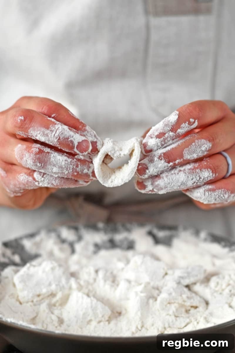 Two hands are dredging a calamari ring in a shallow dish filled with grain-free flour, ensuring a thorough and even coating for maximum crispiness.
