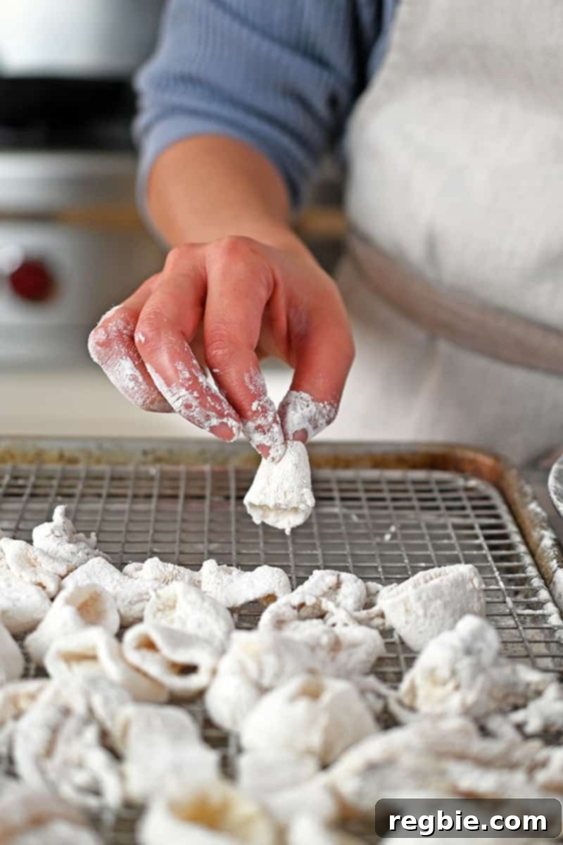 A hand is adding dredged calamari rings to a rack on a rimmed baking sheet, ready for frying or air frying.
