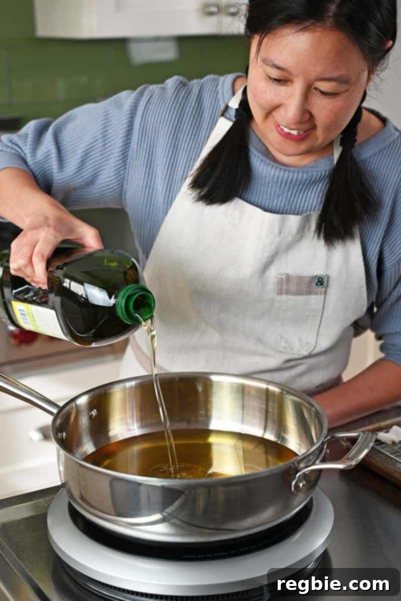 A smiling Asian woman is pouring avocado oil into a pot on an induction cooktop, preparing for deep frying calamari.