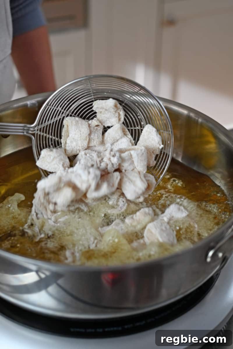A spider strainer is adding paleo calamari to a large pot of hot oil, illustrating the deep frying process.