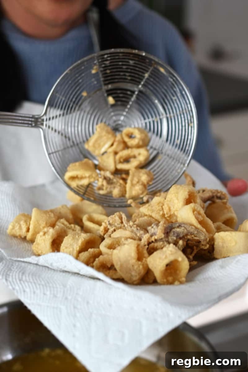 Transferring golden brown paleo fried calamari with a strainer to a paper-towel lined plate for draining excess oil.