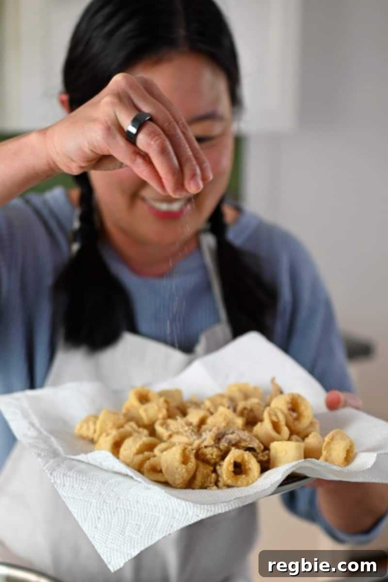 A smiling Asian woman is sprinkling salt to a plate of fried calamari, adding the finishing touch to a delicious appetizer.