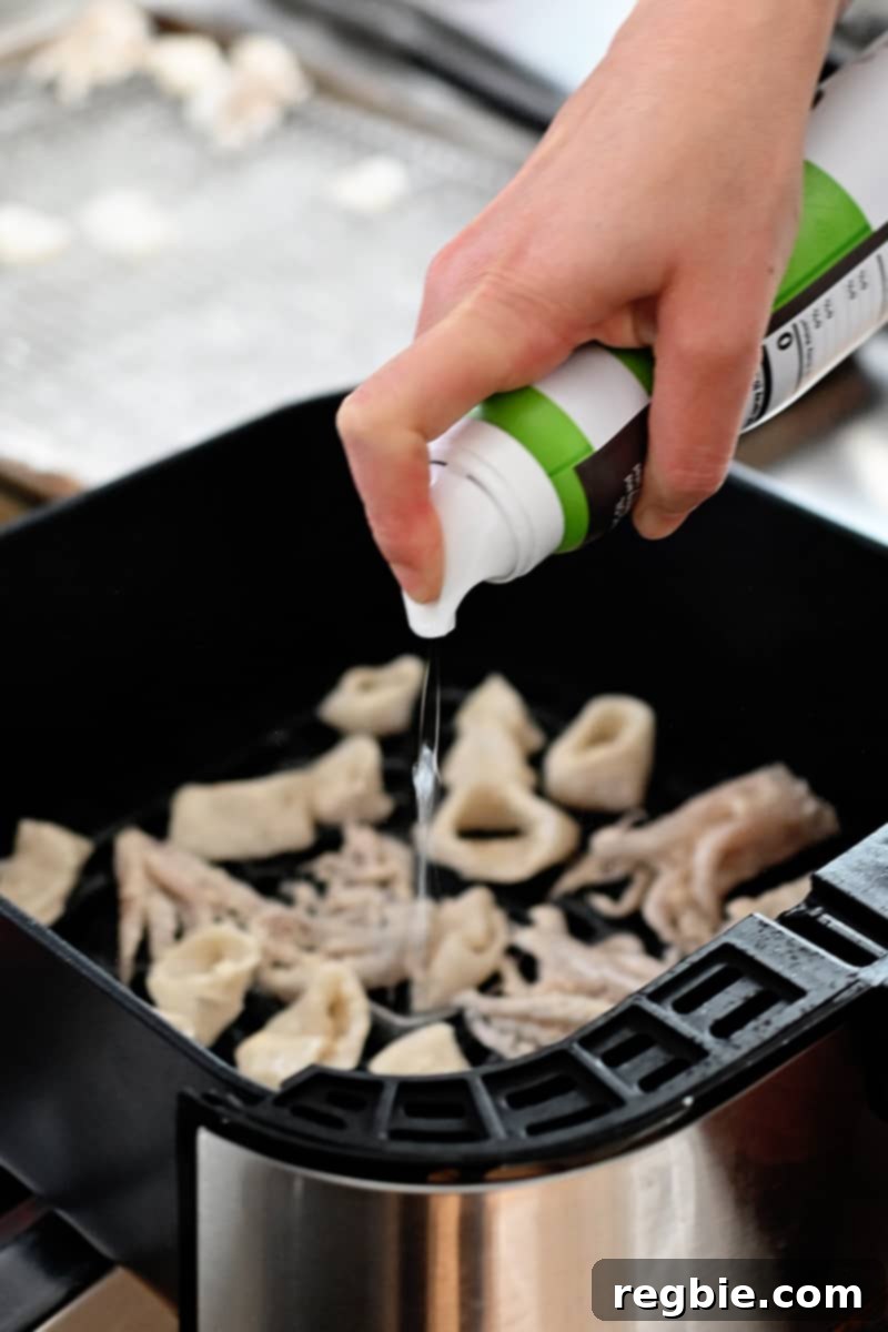 Spraying avocado oil on calamari in an air fryer basket, ensuring even coating for crispy results.