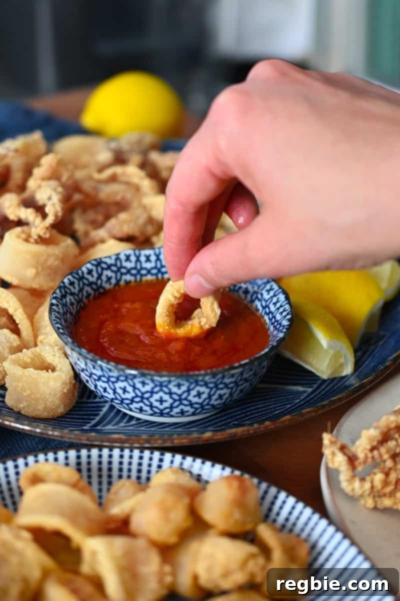A hand dipping paleo and gluten-free fried calamari in a bowl of marinara sauce, highlighting the crunchy texture and delicious pairing.