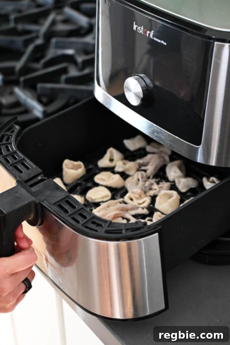 A hand is closing an air fryer filled with calamari, ready to be cooked to crispy perfection.