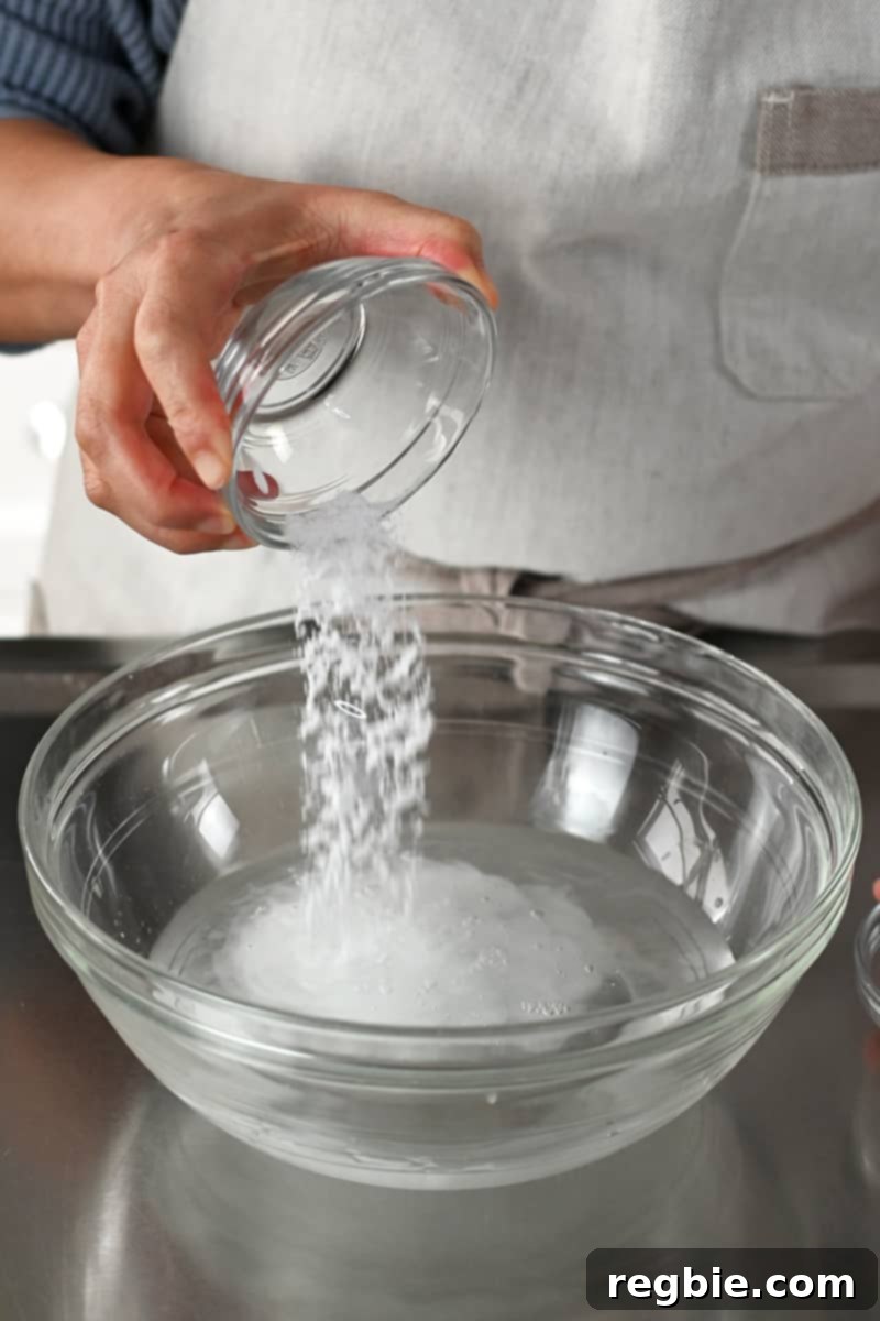 Adding salt to a glass bowl filled with water and baking soda to make an alkaline brine, illustrating the tenderizing process.