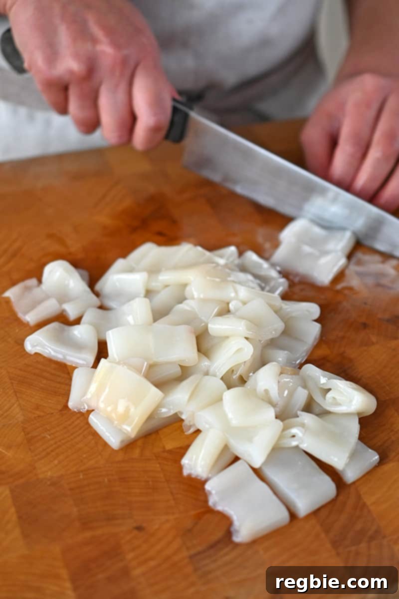 Slicing cleaned calamari into 3/4-inch rings on a wooden cutting board, preparing for tenderization and frying.