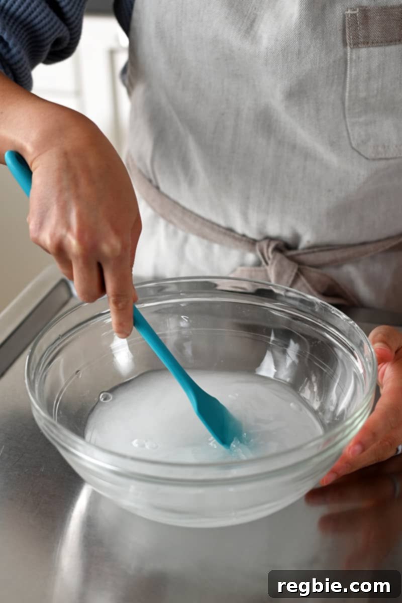 A blue silicone spatula is stirring a salt solution in a clear bowl, showing the preparation of the tenderizing brine.