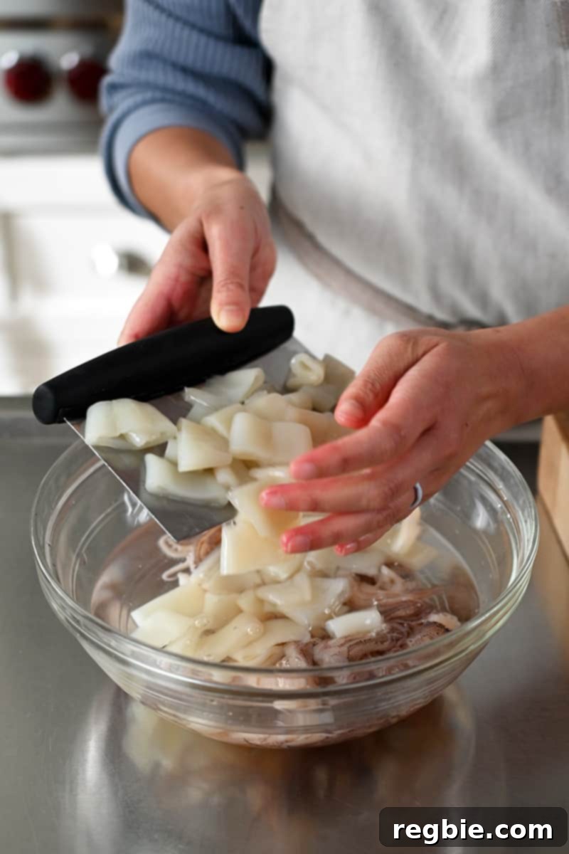 Two hands are adding sliced calamari to a clear bowl filled with a clear liquid, demonstrating the brining step.