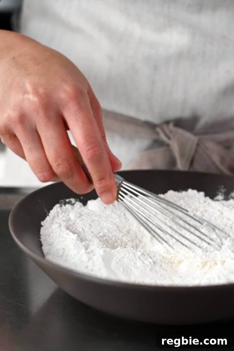A hand is using a whisk to mix flour in a shallow brown bowl, preparing the gluten-free coating for calamari.