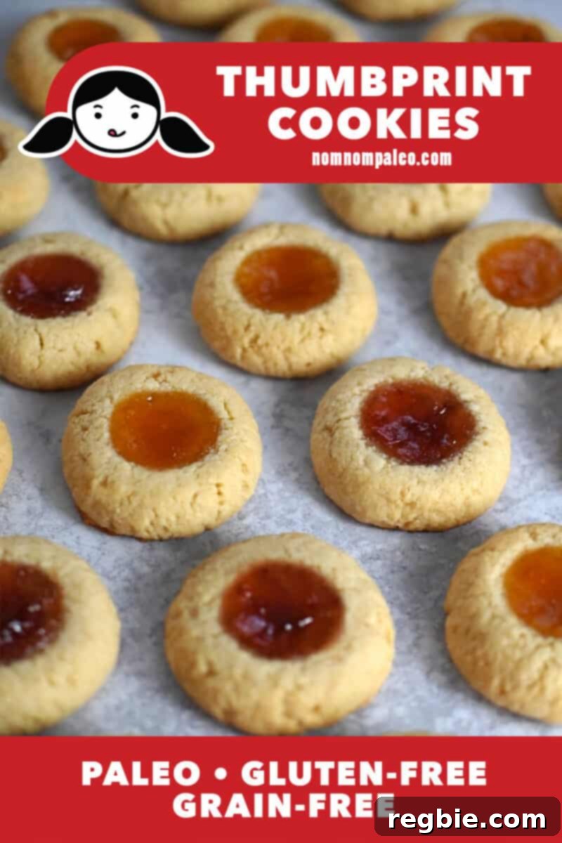 An overhead shot of paleo thumbprint cookies on a marble background, showcasing their golden edges and vibrant jam centers. A red banner highlights them as paleo, gluten-free, and grain-free.