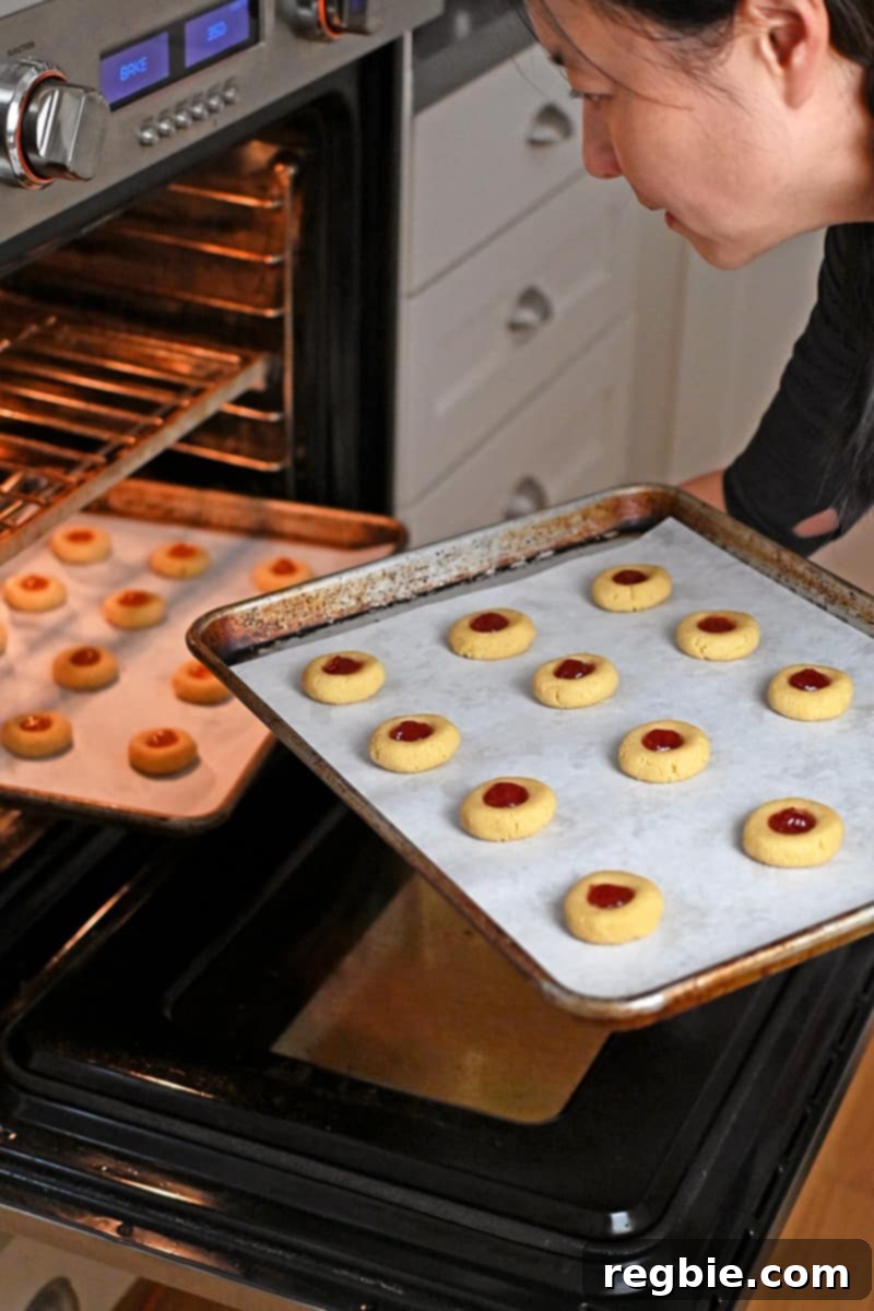 An Asian woman carefully removes a tray of perfectly baked paleo thumbprint cookies from the oven.