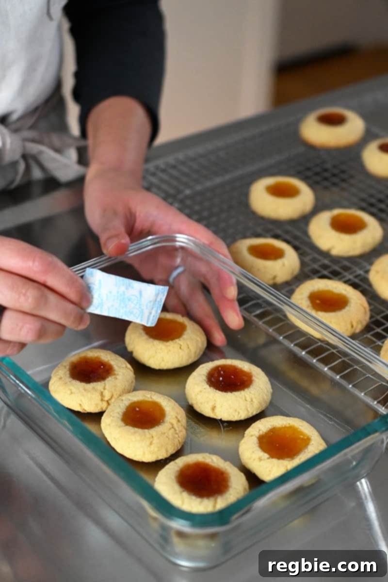 A hand is carefully adding a silica gel packet into a glass container filled with delicious paleo thumbprint cookies for extended freshness.