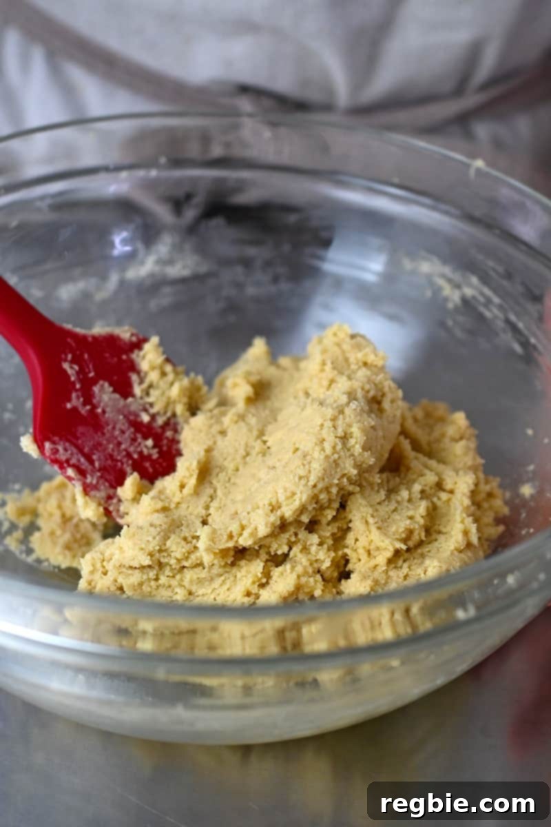 The pale cookie dough is being mixed in a glass bowl with a red silicone spatula, ready to be chilled.
