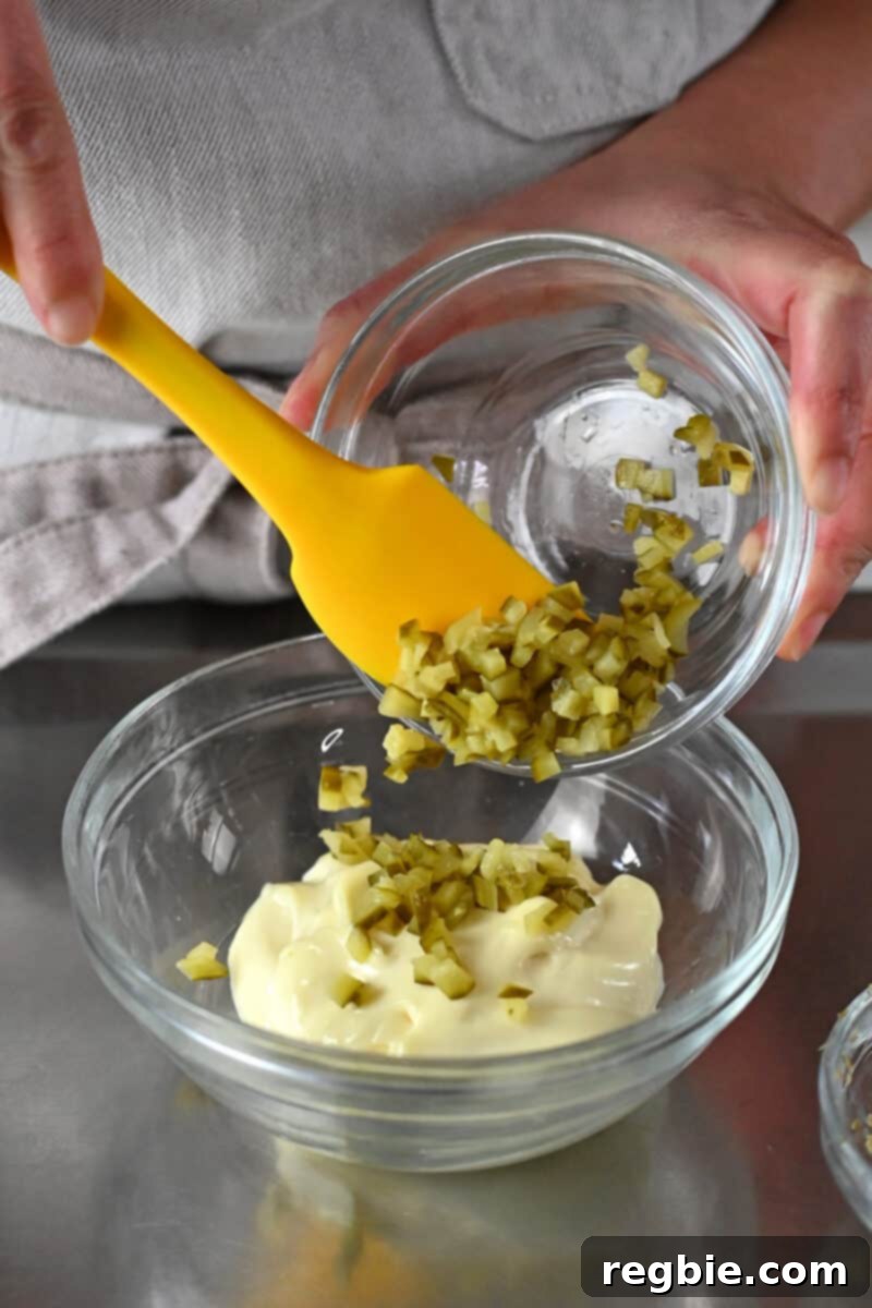 Whip Up Perfect Homemade Tartar Sauce 4 Adding diced pickles to a glass bowl filled with mayonnaise.