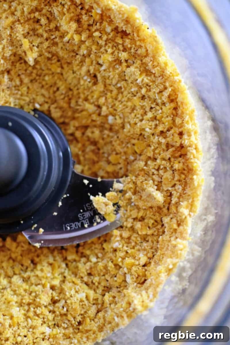 An overhead shot showing golden plantain chip crumbs in an open food processor, ready to be used as a gluten-free coating for fish sticks.