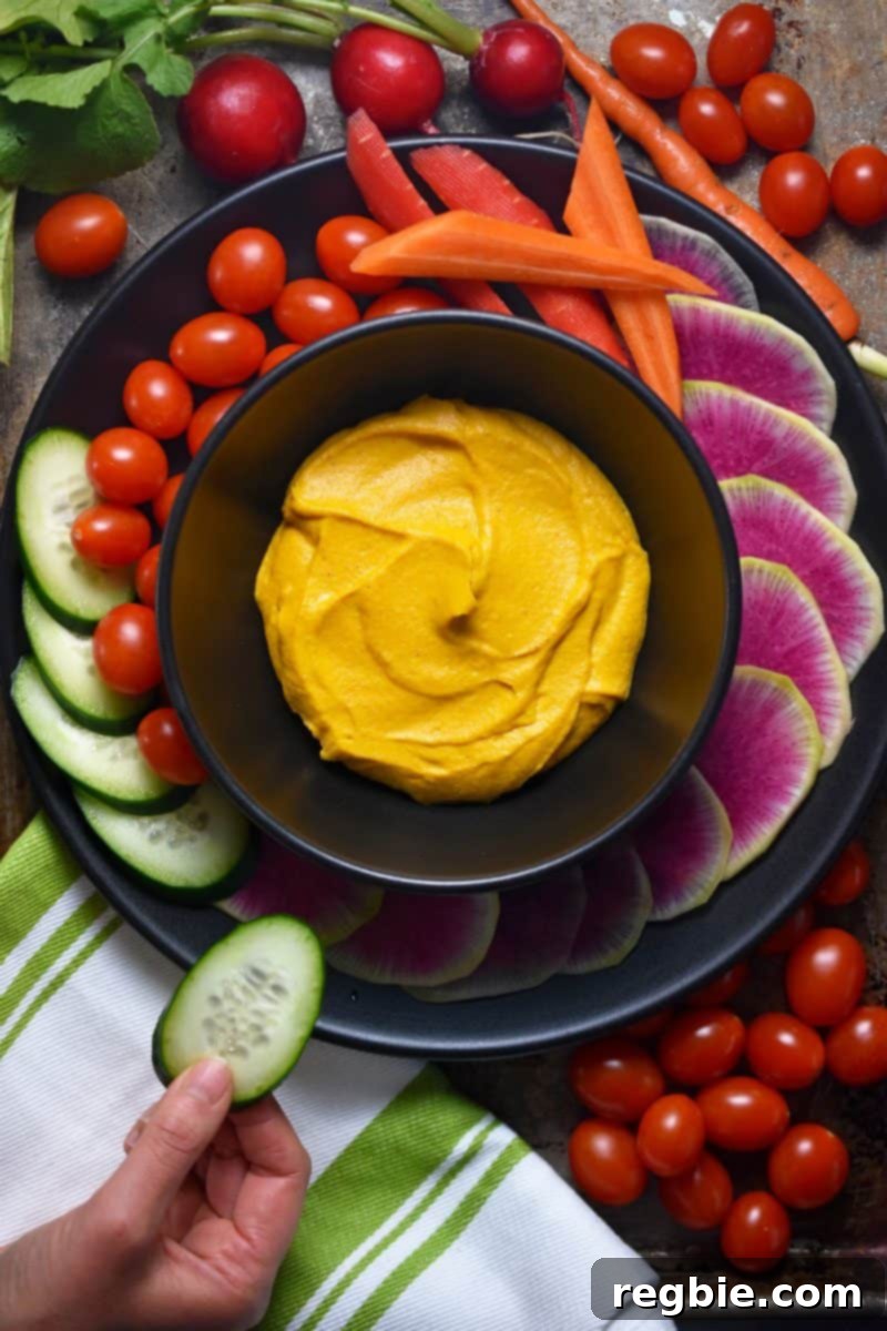 A bowl of sweet potato cashew dip with an array of vegetables arranged around the bowl.