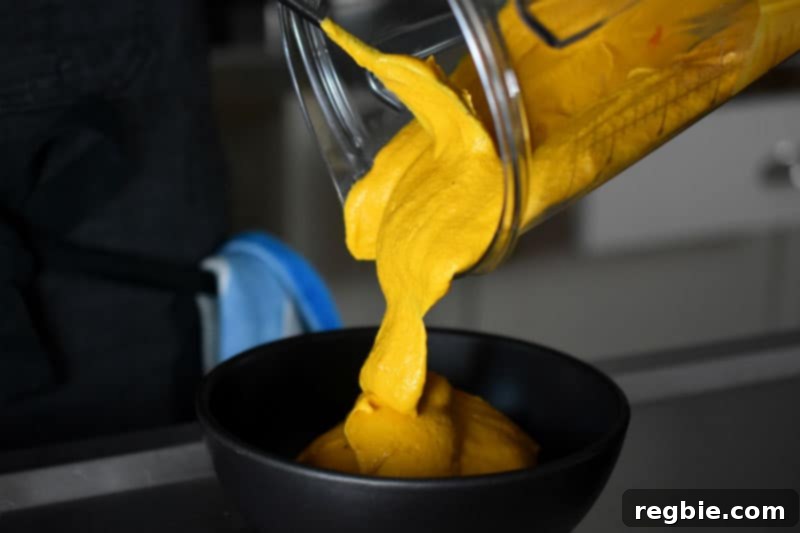 Someone pouring the bright orange-yellow sweet potato and cashew dip into a bowl.