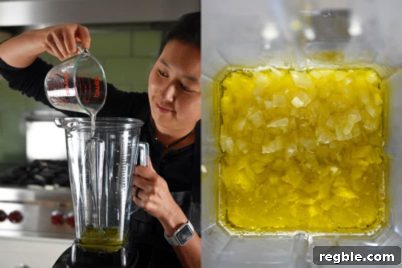 Someone pouring oil into a blender with the cooked onions and garlic.