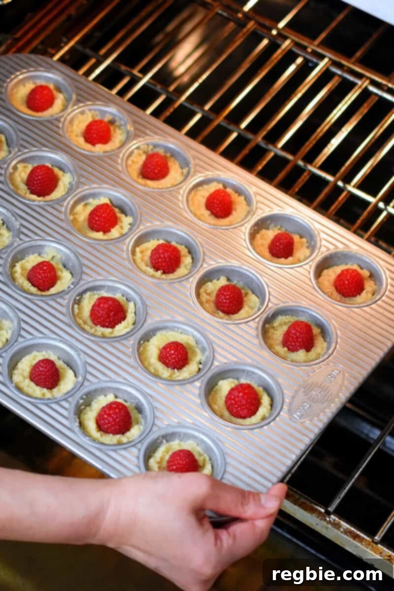 Paleo Raspberry Financiers 11 A mini muffin pan, brimming with unbaked raspberry financiers, is carefully slid into a preheated hot oven, ready for baking.