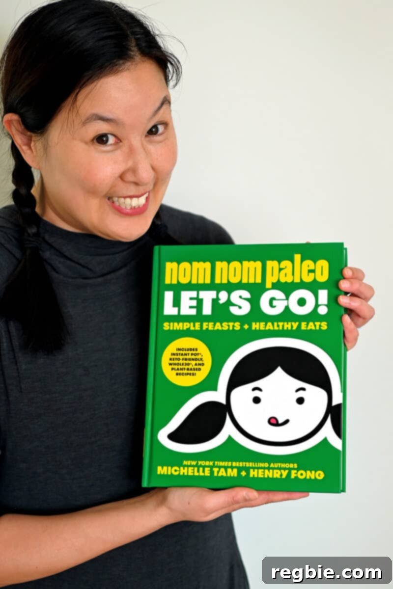 Paleo Raspberry Financiers 3 A vibrant and engaging photo of Michelle Tam, a smiling Asian woman, proudly holding up her green-covered cookbook titled