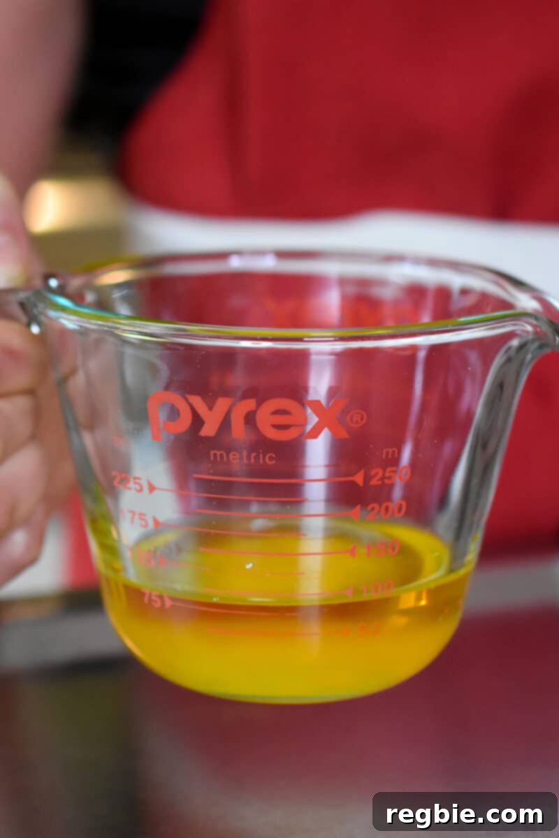 Paleo Raspberry Financiers 4 A hand holds a clear liquid measuring cup, showcasing the perfectly melted ghee, ready to be cooled to room temperature for the paleo financier recipe.