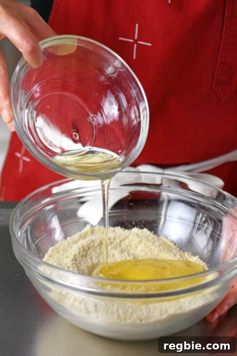 Paleo Raspberry Financiers 7 A stream of lightly whisked egg whites pours into a glass mixing bowl, where it will be combined with the dry ingredients for the paleo and gluten-free financiers batter.