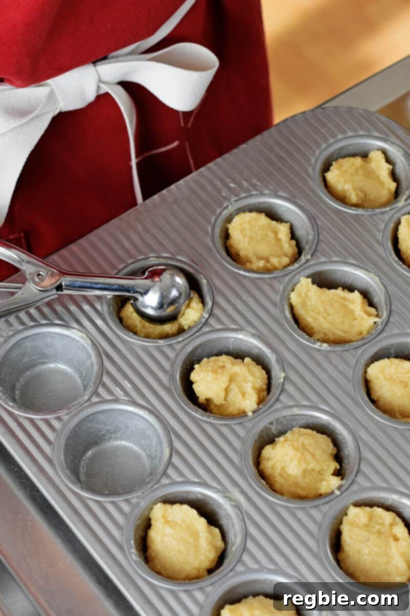 Paleo Raspberry Financiers 9 A small scoop delivers a perfect portion of paleo financier batter into a greased mini muffin pan, demonstrating precise batter distribution.