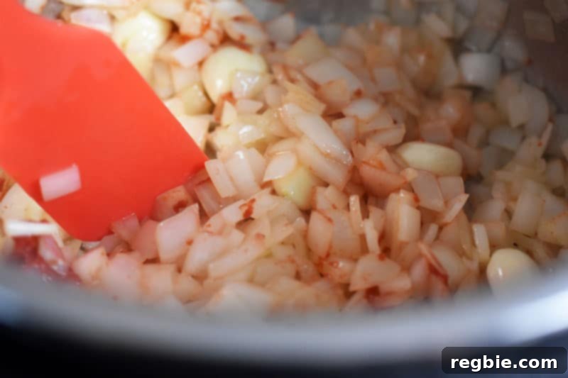 A close-up shot of chopped onions and rich tomato paste sautéing together in the Instant Pot, developing deep flavors.