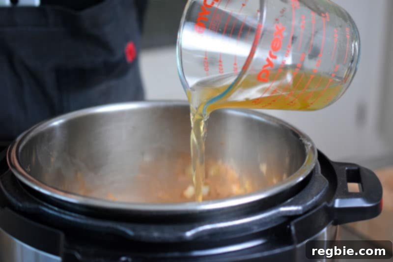 A steady stream of chicken broth pours from a liquid measuring cup into the Instant Pot, deglazing the pot.