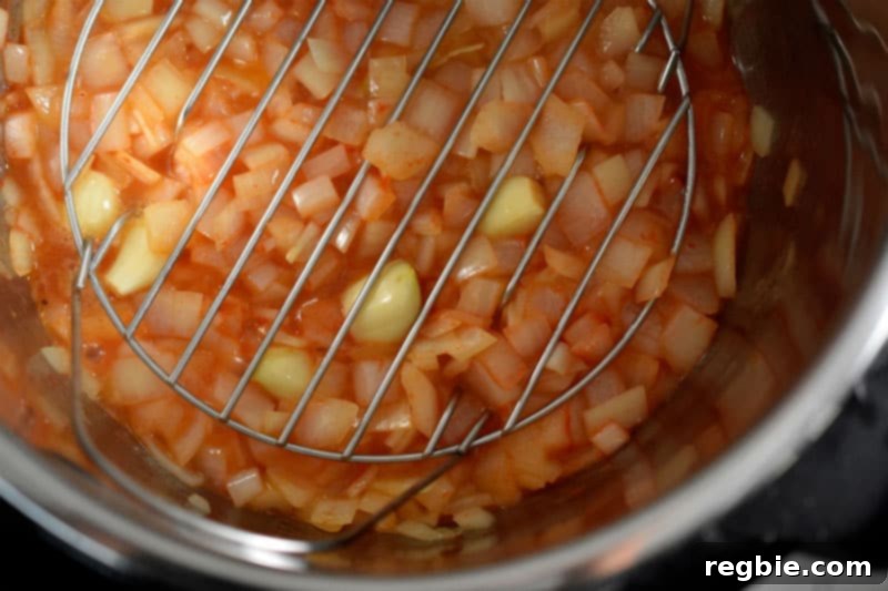 A stainless steel steaming rack being carefully placed on top of the sautéed onions and garlic in an Instant Pot.